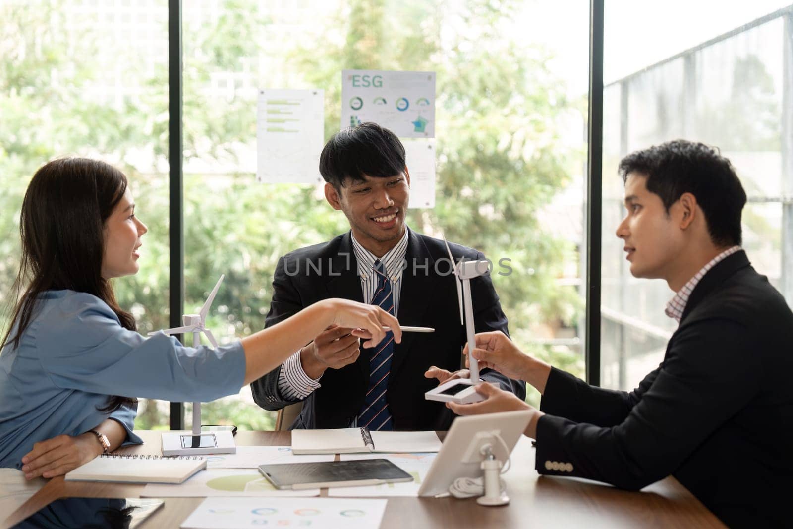 A team of diverse professionals engaging in a sustainable ESG meeting, discussing charts and renewable energy models with enthusiasm and collaboration.