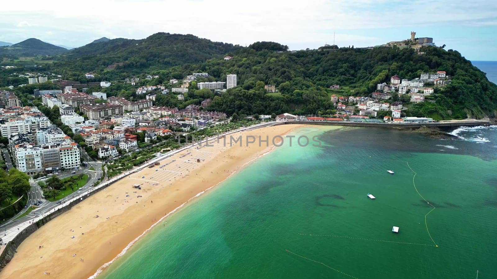 This aerial shot captures a charming coastal town by a sandy beach and the vibrant blue ocean waters