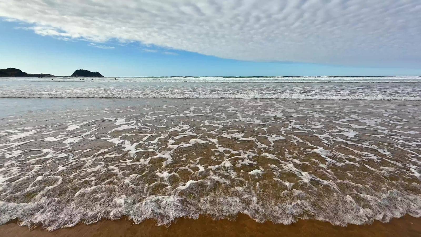 This scene captures a tranquil beach featuring gently rolling waves under a beautiful, peaceful, cloudy sky