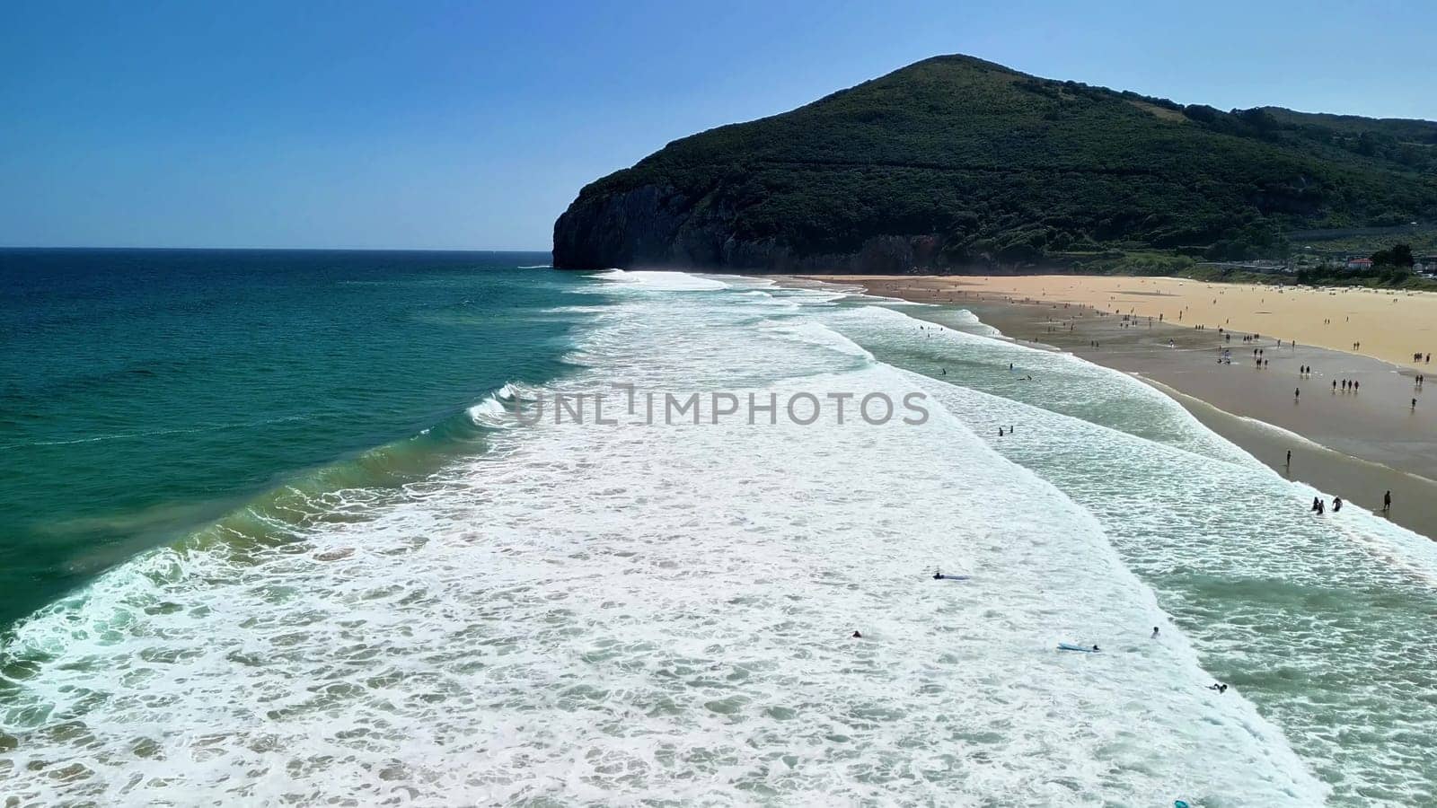The beautiful coastline features waves crashing on the sandy beach, creating picturesque scenery with clear blue waters