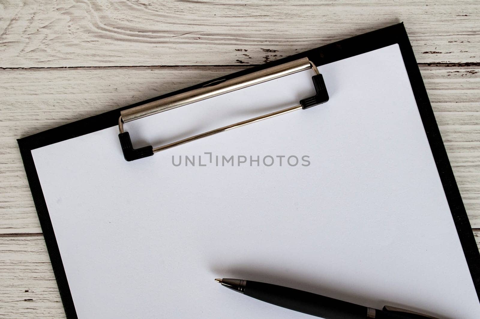 Top view of a blank clipboard with a sheet of white paper and a black pen. Copy space concept.