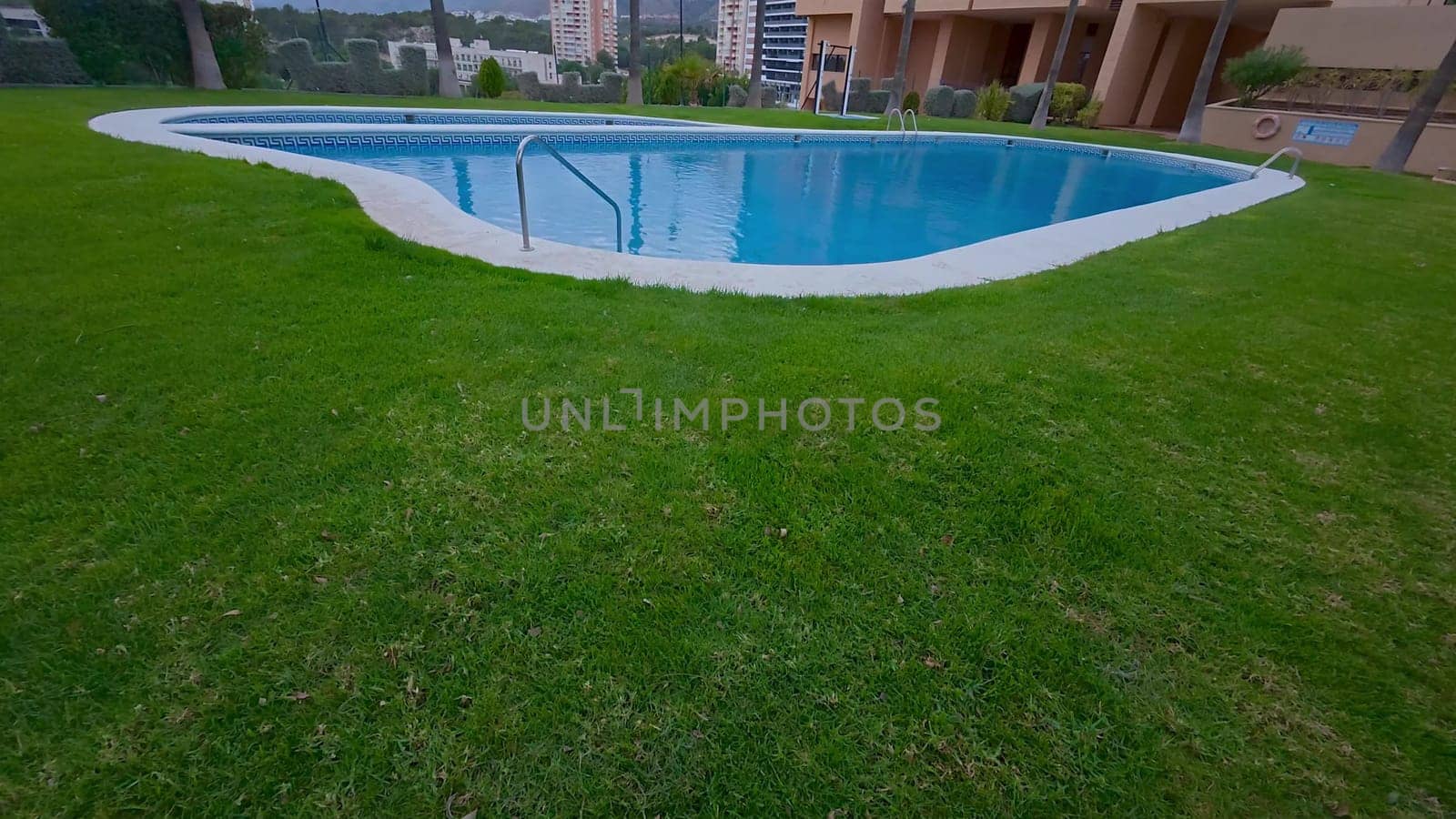 A serene swimming pool is surrounded by a vibrant green lawn in a modern residential area, offering comfort