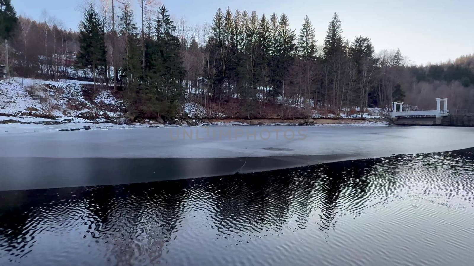 A tranquil winter landscape that beautifully showcases a frozen lake surrounded by tall evergreen trees