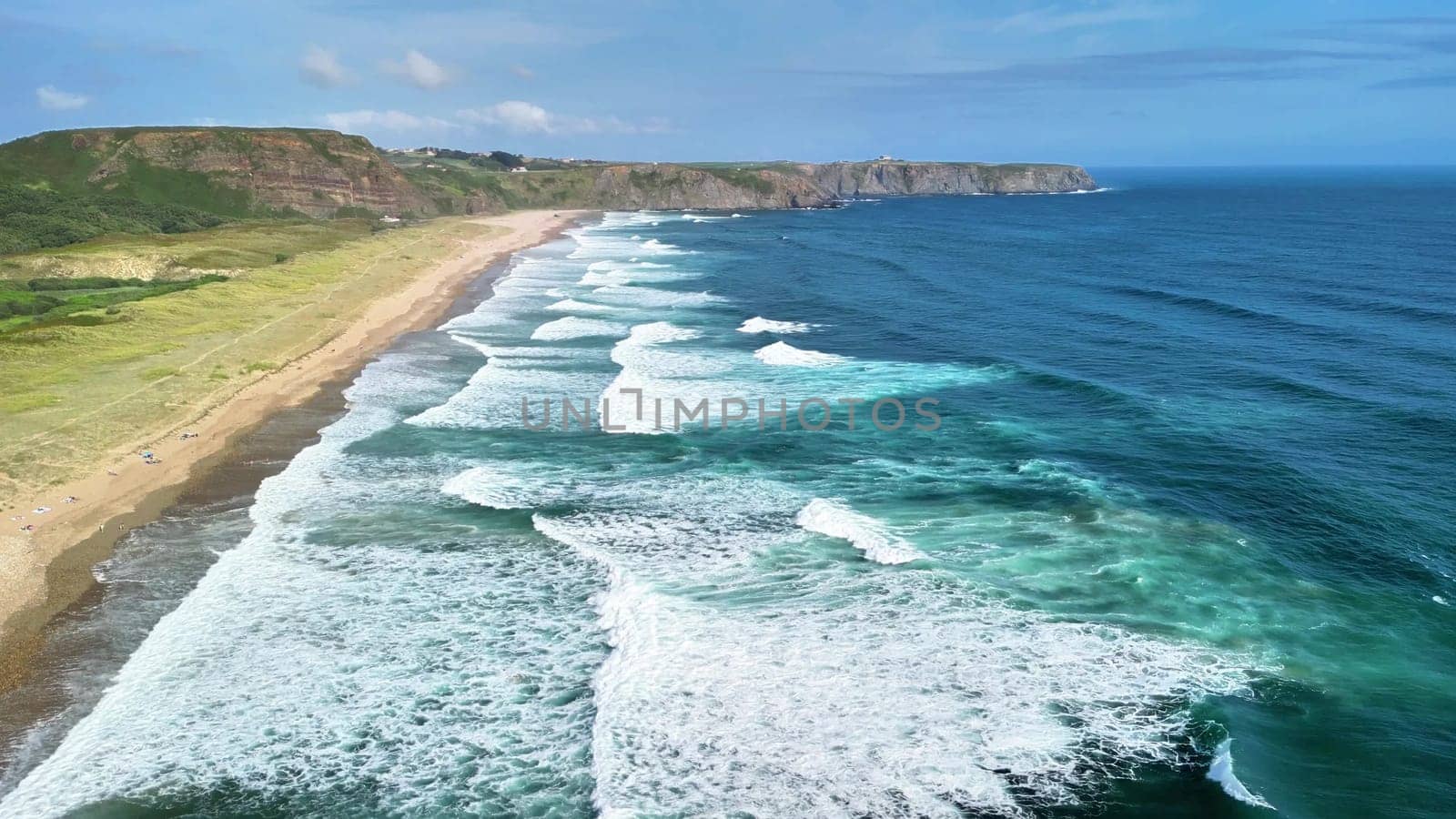 A breathtaking coastal scene showcases vibrant blue waves crashing powerfully on golden sands under a clear, bright sky