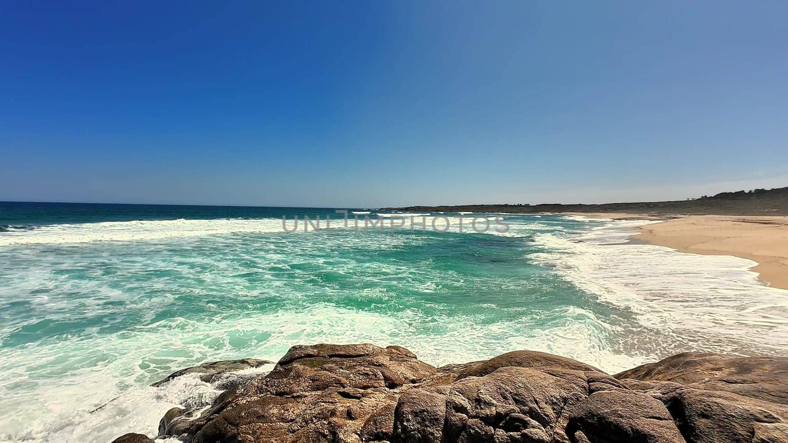 A breathtaking beach scene showcasing gentle waves and crystal-clear waters under a vibrant blue sky.