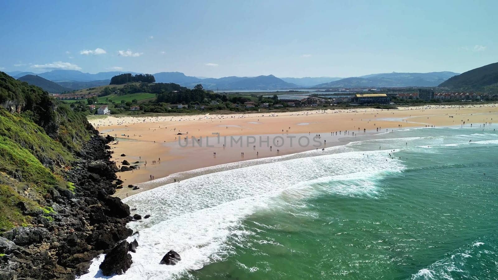 Stunning aerial view showcasing a serene beach, tranquil waves, sunbathers, and lush, vibrant scenery all around