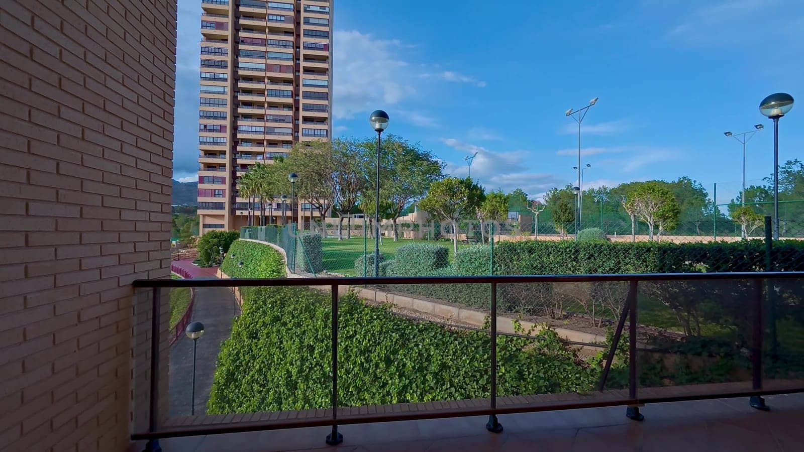 A modern balcony view overlooking a vibrant urban park with greenery and a stylish residential building