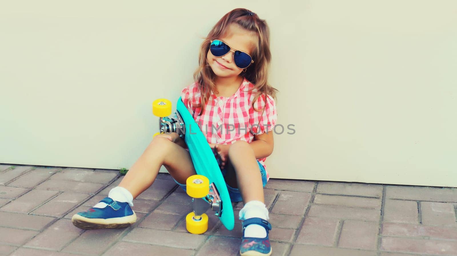 Portrait of stylish little girl child posing with skateboard on city street