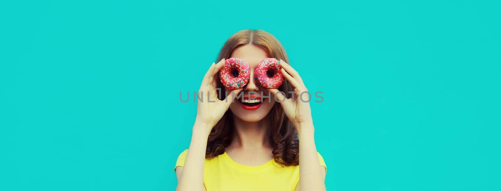 Portrait of happy cheerful smiling young woman with sweet donut having fun isolated on blue studio background
