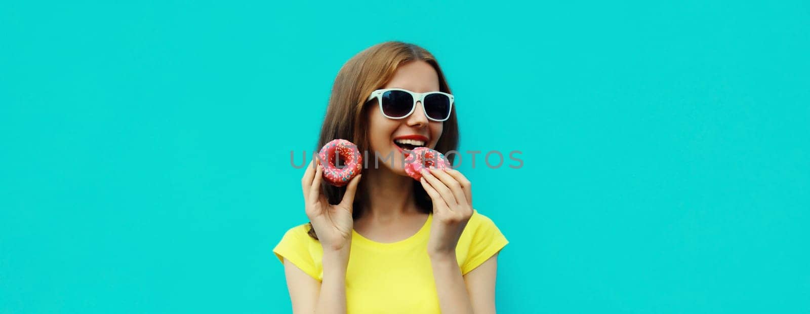 Portrait of happy cheerful smiling young woman with sweet donut having fun isolated on blue studio background