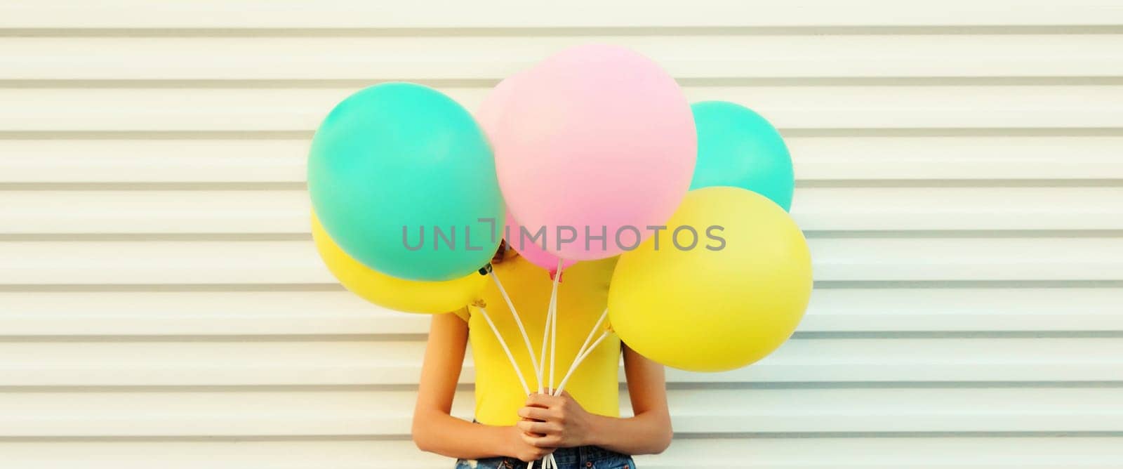 Summer, holiday, celebration, happy cheerful woman covering her head with bright colorful balloons having fun on white wall background