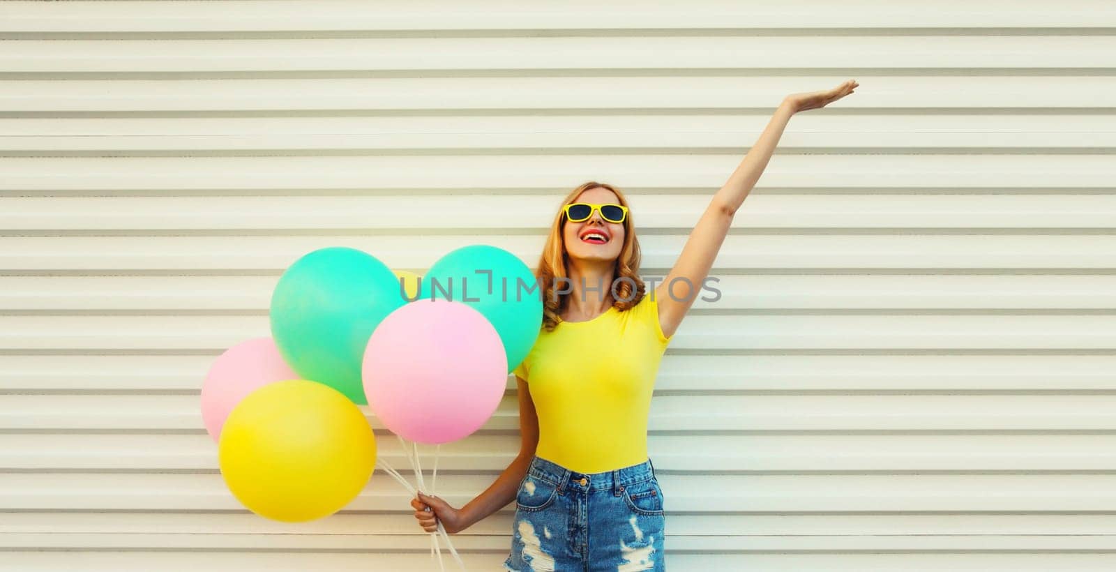 Summer, holiday, celebration, happy cheerful young woman with bright colorful balloons having fun on white wall background
