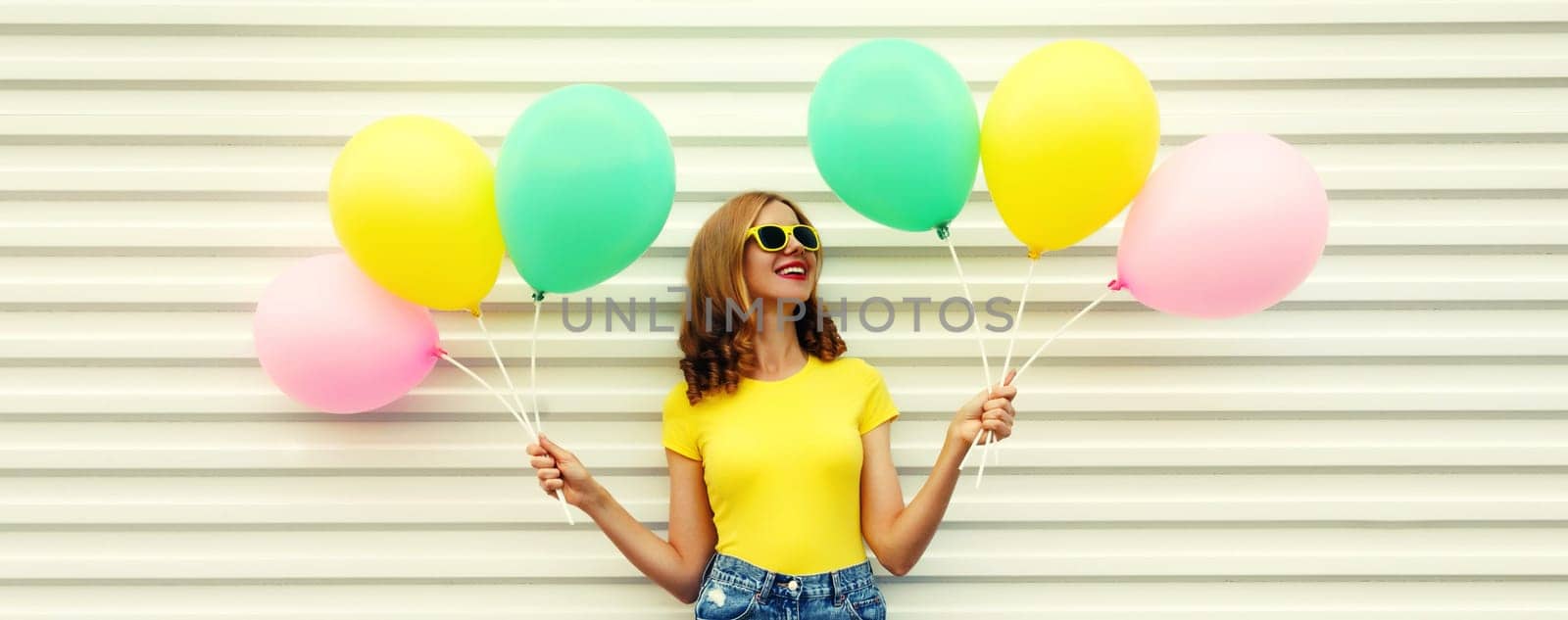 Summer, holiday, celebration, happy cheerful young woman with bright colorful balloons having fun on white wall background