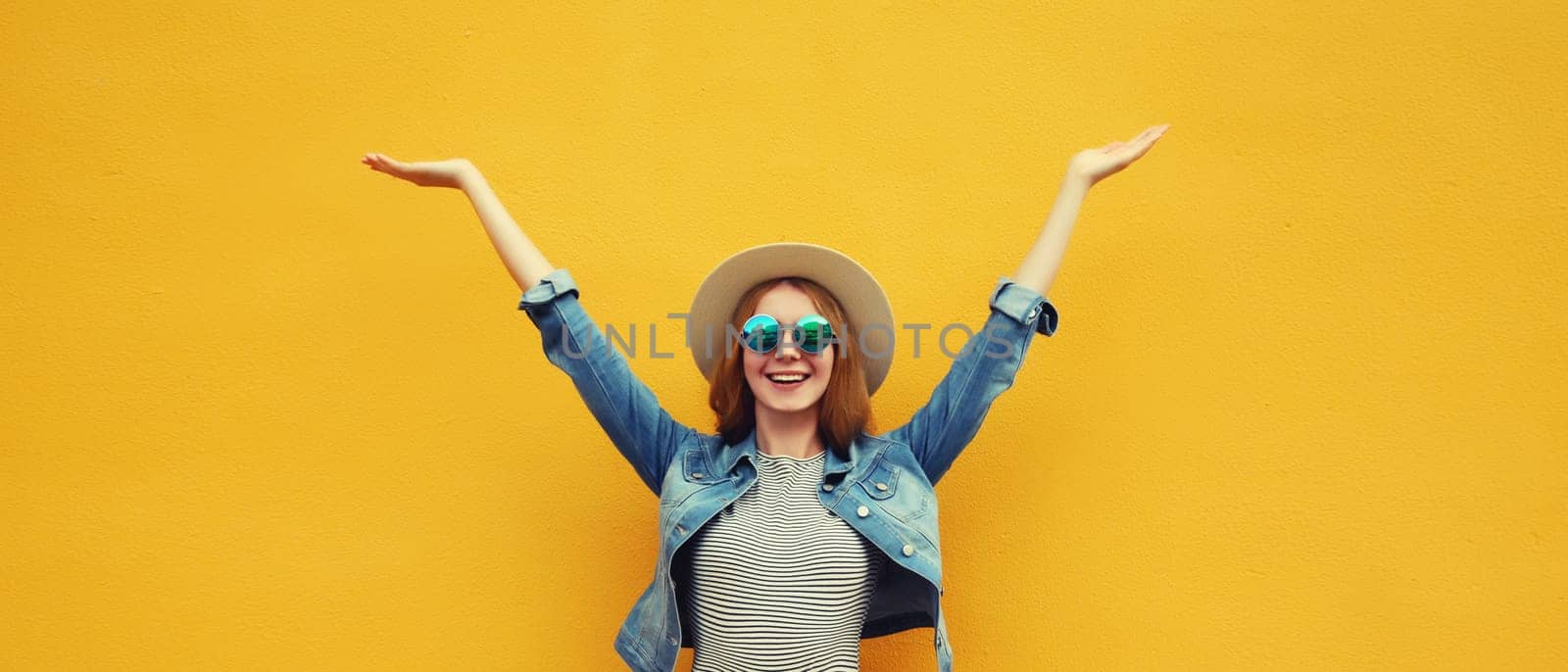 Summer holidays, inspired happy cheerful smiling young woman raising her hands up wearing denim clothing, straw hat on colorful yellow background