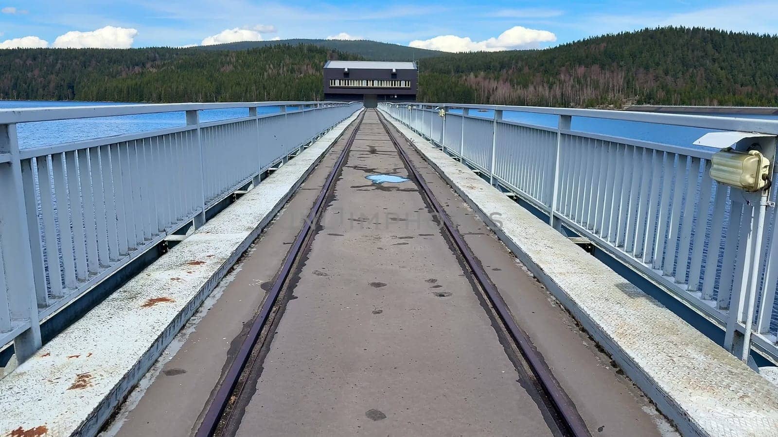 A serene view of a bridge crossing tranquil water, surrounded by vibrant nature and bright blue skies
