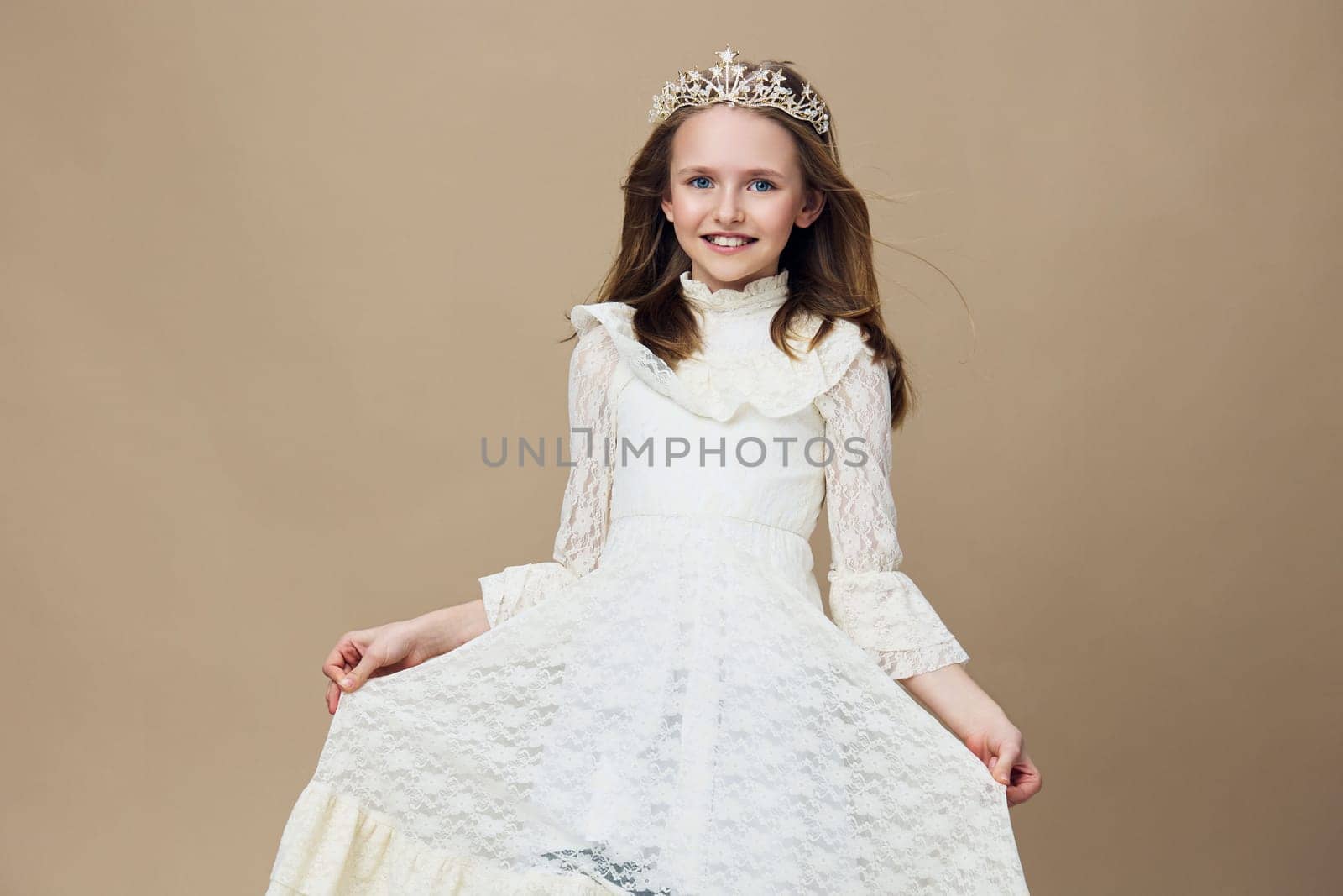 A joyful young girl wearing a stunning white dress and a tiara, exuding happiness against a soft beige background, ideal for themes of childhood, elegance, and special occasions