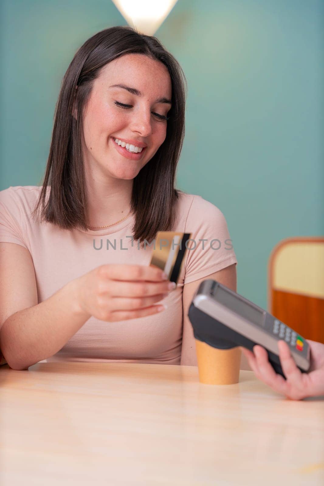 African American and Caucasian women smiling while paying at a coffee shop. One holds a card, the other a phone. Concept of friendship, technology, and casual lifestyle in a modern setting. Vertical