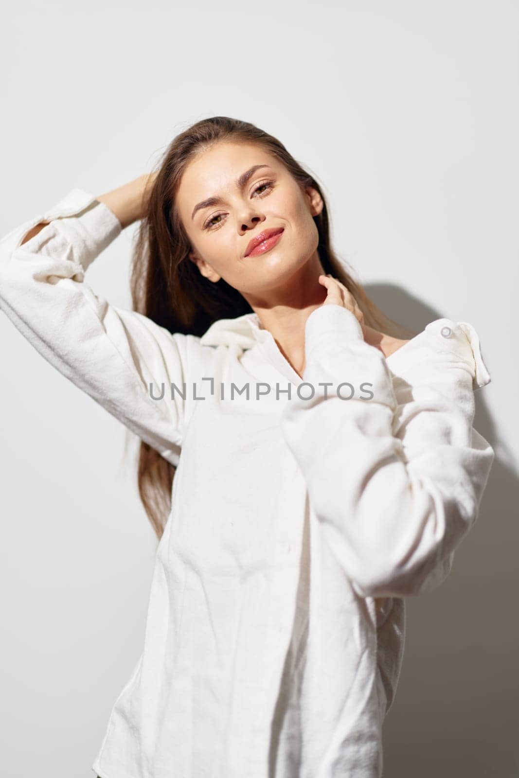 A cheerful young woman poses against a plain light background, dressed in a white shirt Her relaxed expression and natural beauty convey confidence and positivity, making the image ideal for lifesty