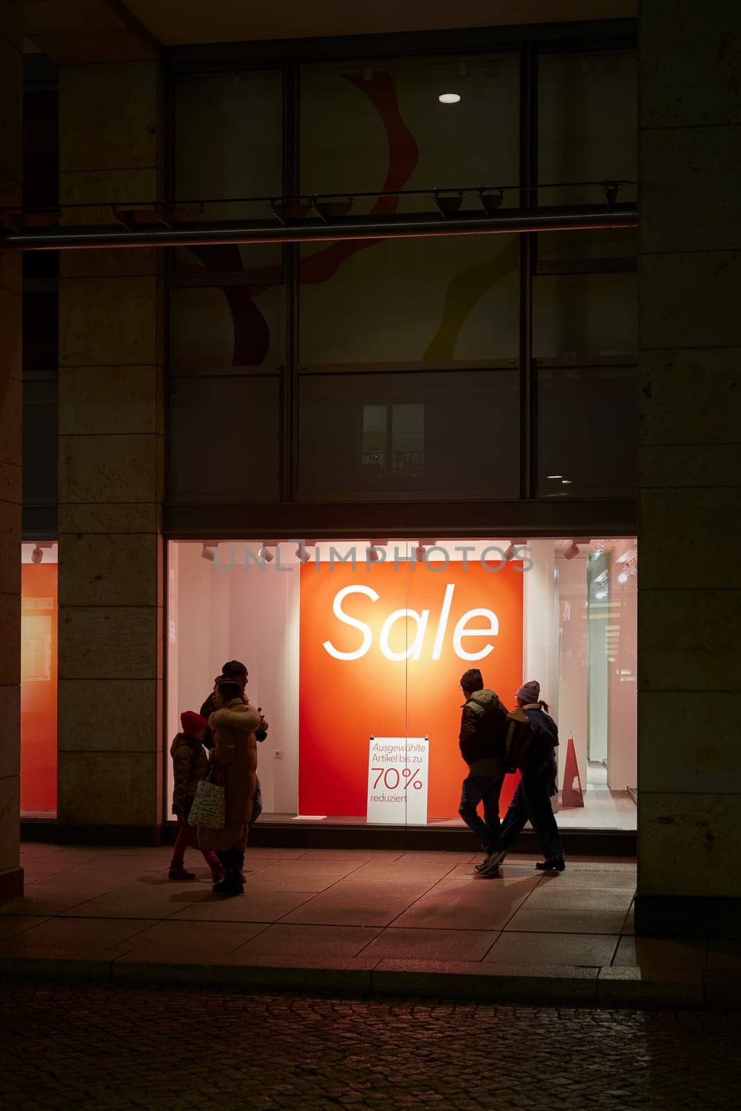 Dresden, Germany – January 18, 2025: Passers-by window shopping in the evening and a sign with the inscription Sale