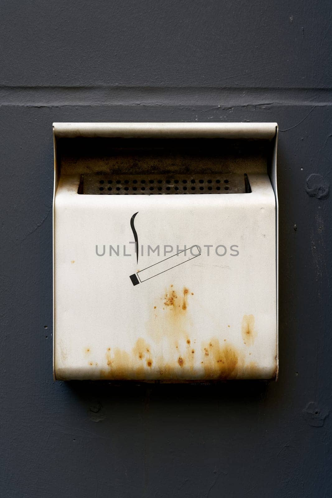 Container for cigarettes, ashtray on a house wall at a smoking area