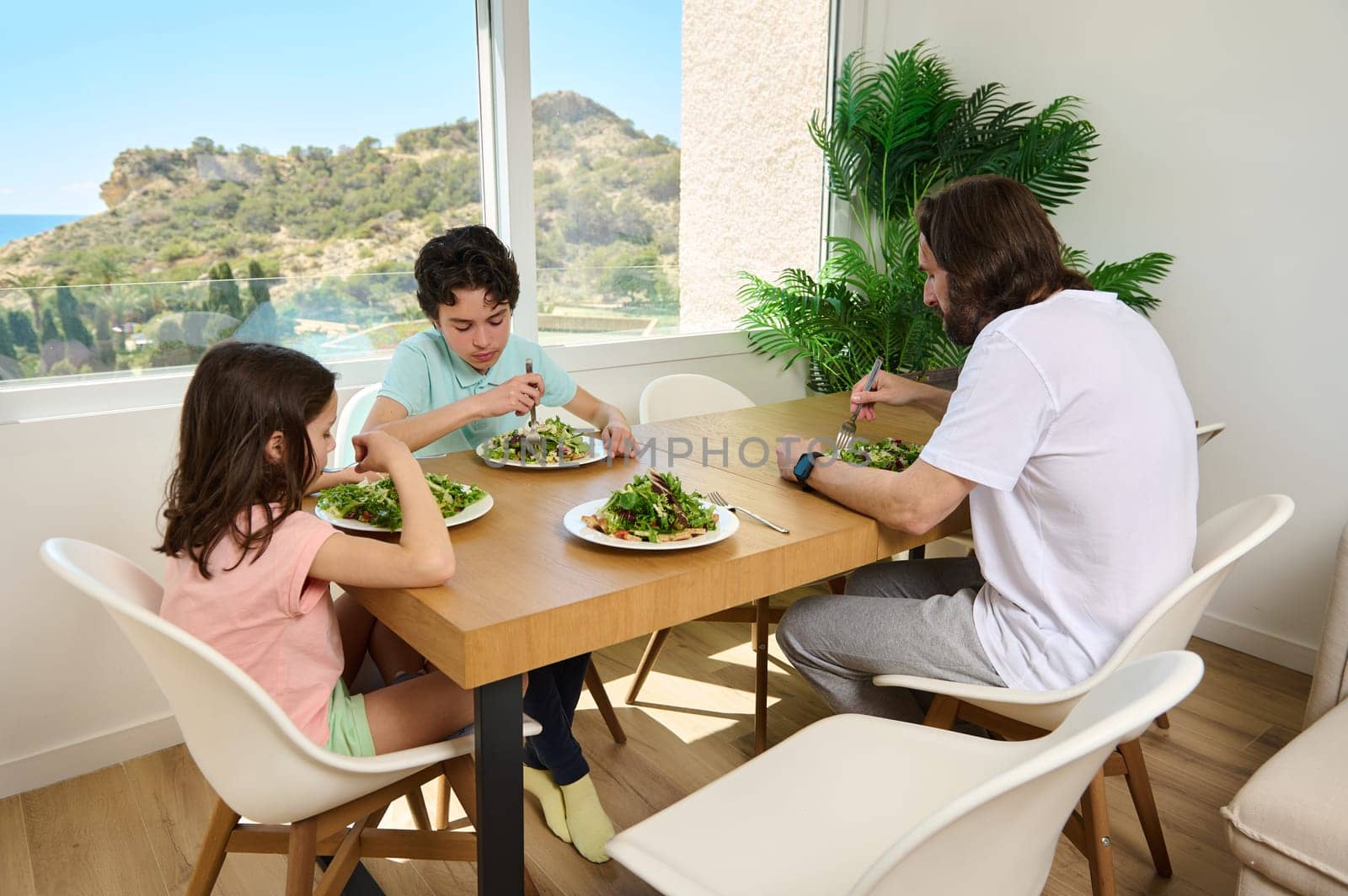 A family shares a balanced meal in a contemporary bright dining area overlooking lush greenery.