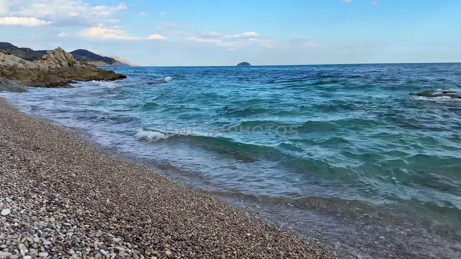 A truly stunning coastal view showcasing gentle waves lapping at a pebbly beach beneath a clear, sunny blue sky