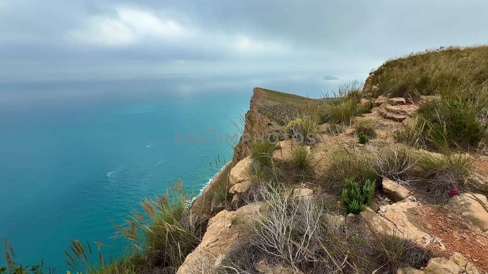The stunningly beautiful scenery showcases a rugged cliff edge, with a vibrant blue ocean flowing beneath cloudy skies