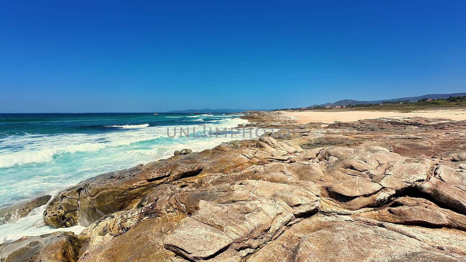 An enchanting coastal scene showcasing majestic rocks, gentle ocean waves, and a beautifully clear blue sky