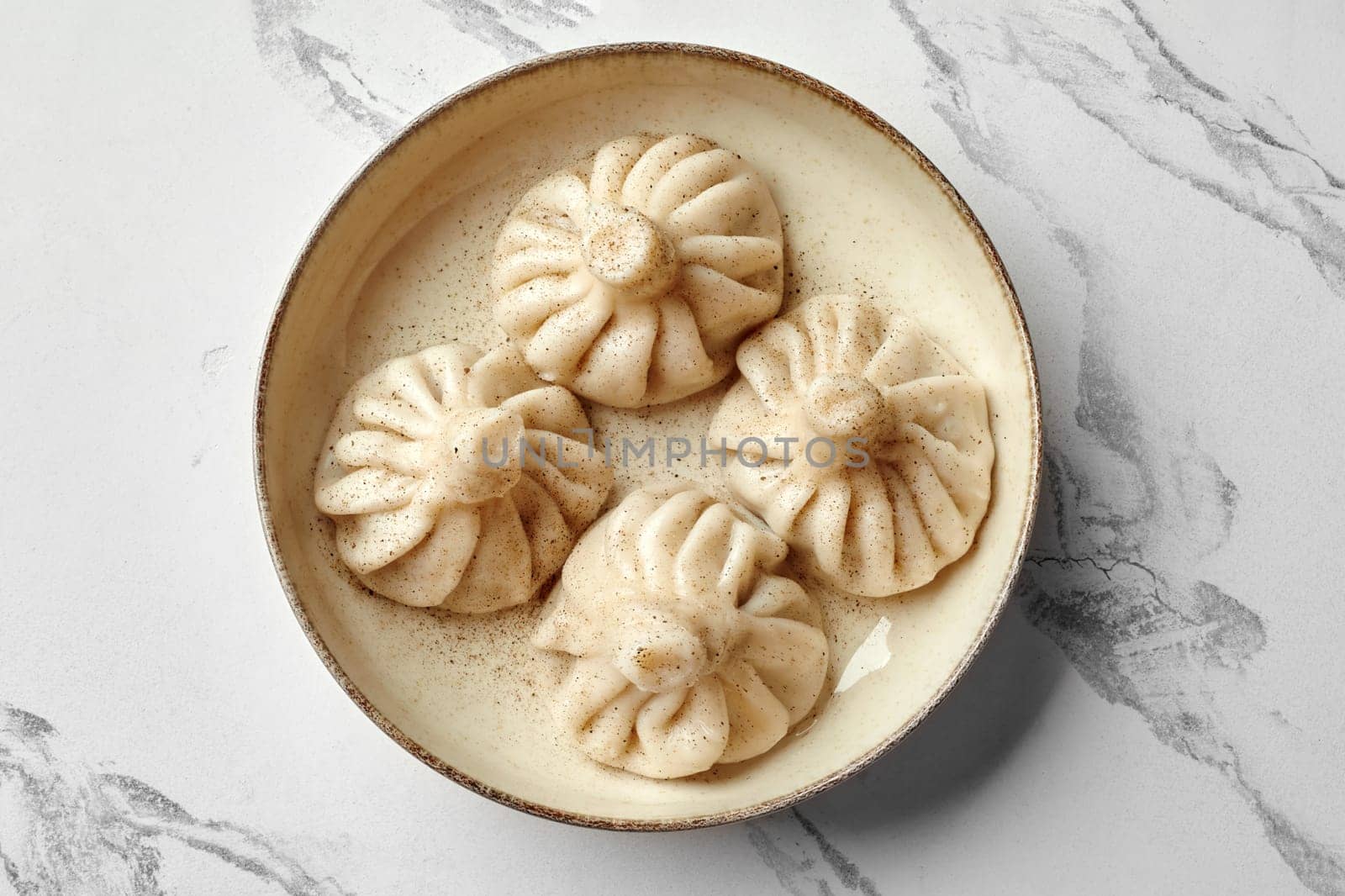 Four khinkali, georgian dumplings, seasoned with black pepper, served on a ceramic plate on a marble table