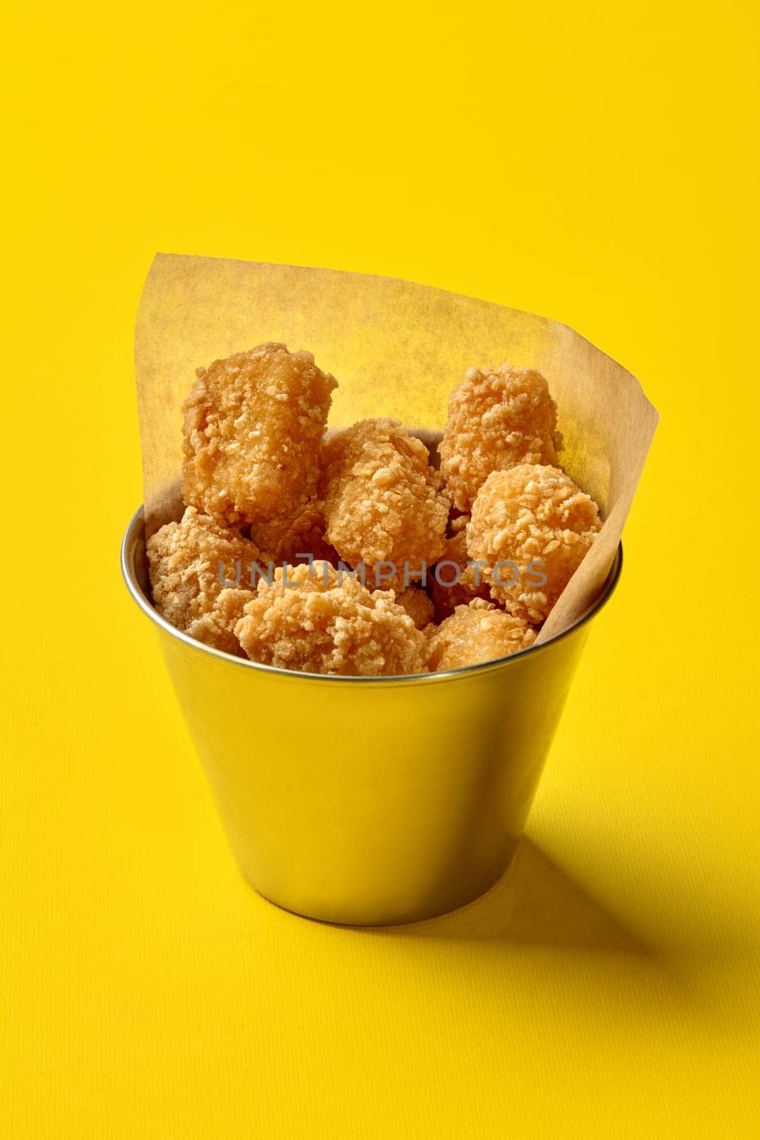 Breaded tater tots overflowing a metal bucket on a vibrant yellow background, creating a visually appealing fast food scene