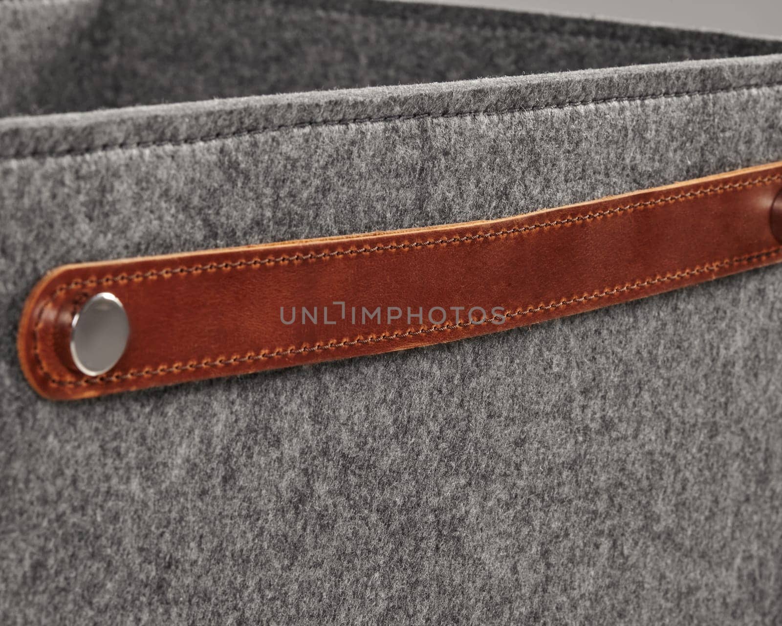 Close-up of brown leather handle attached with metal rivet on grey felt storage basket, highlighting modern and minimalist design