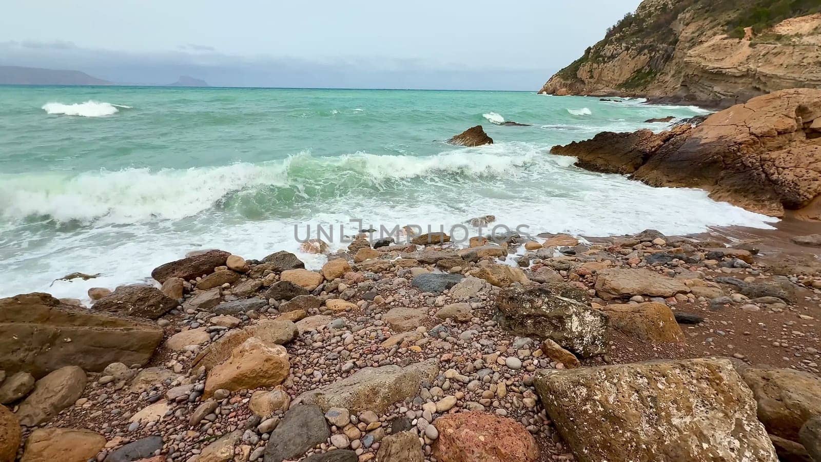A breathtaking and stunning view of powerful waves crashing against a rugged rocky shoreline under a cloudy sky