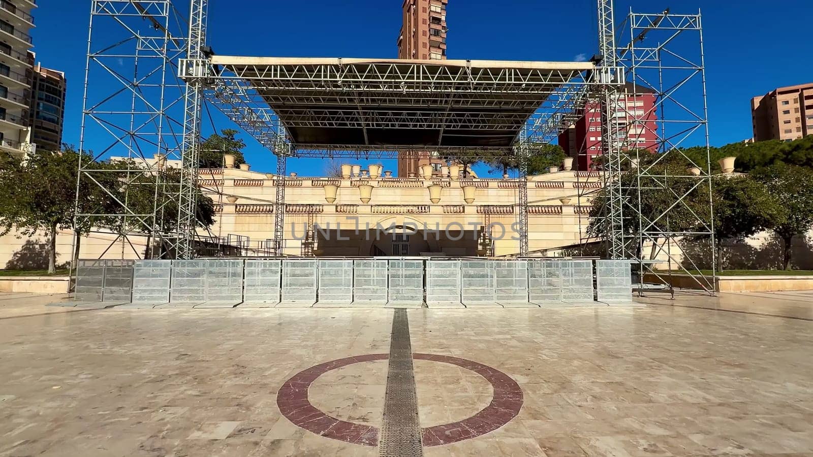 A beautifully prepared concert stage is set amidst city buildings, all under a bright and clear blue sky