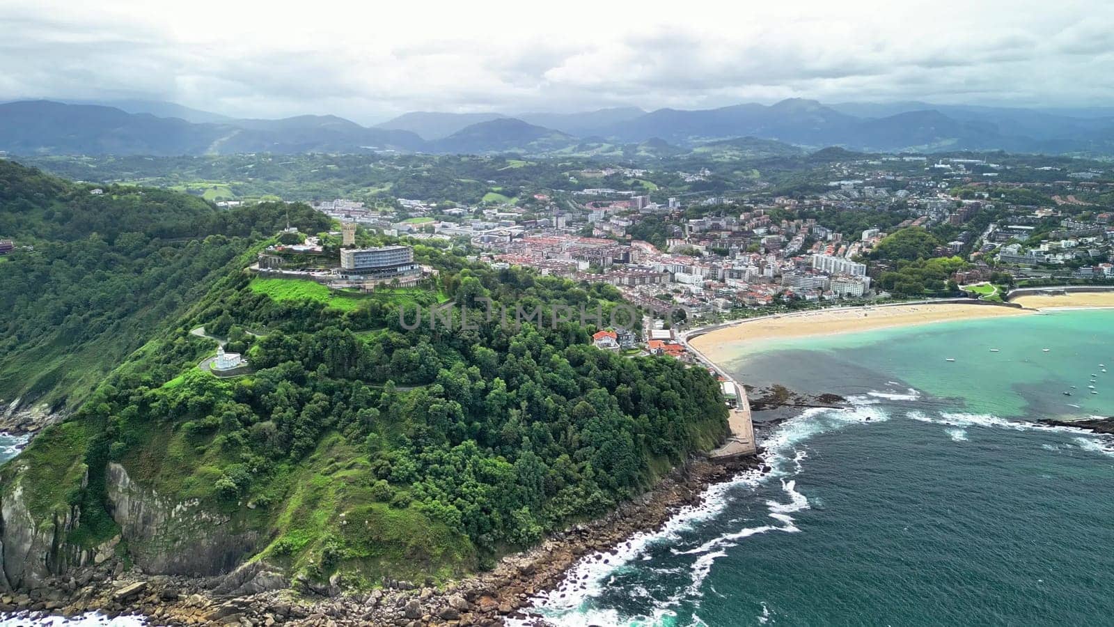 This breathtaking aerial shot captures a gorgeous coastal area with a vibrant green hill and a tranquil beach