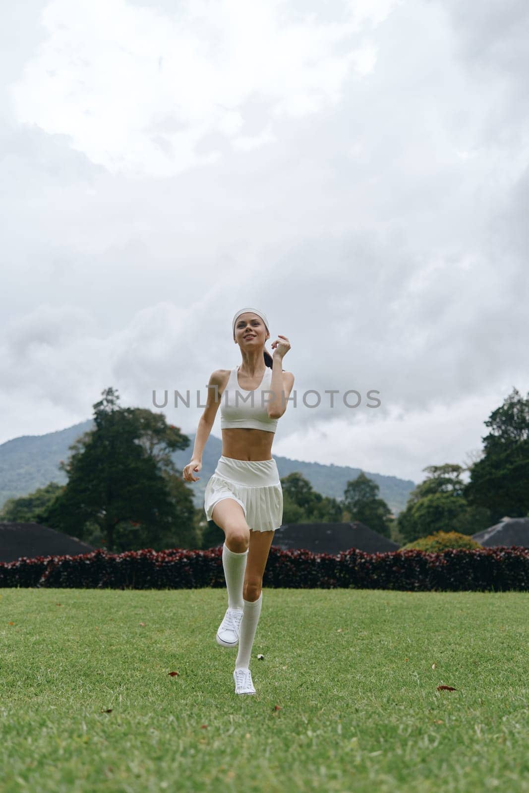 Energetic young woman in a white sports outfit running in a park, showcasing a vibrant outdoor fitness lifestyle, health, and joy