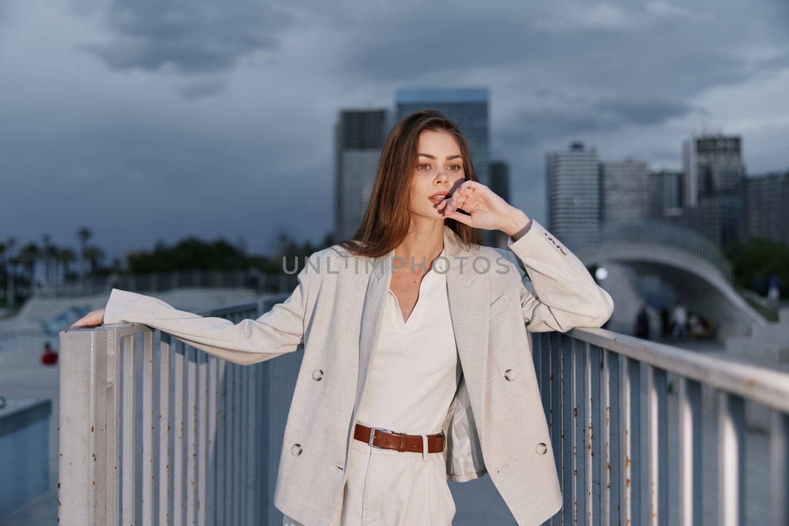 Stylish woman in a beige business outfit poses against an urban skyline, reflecting confidence with a serene, thoughtful expression, ideal for corporate themes.