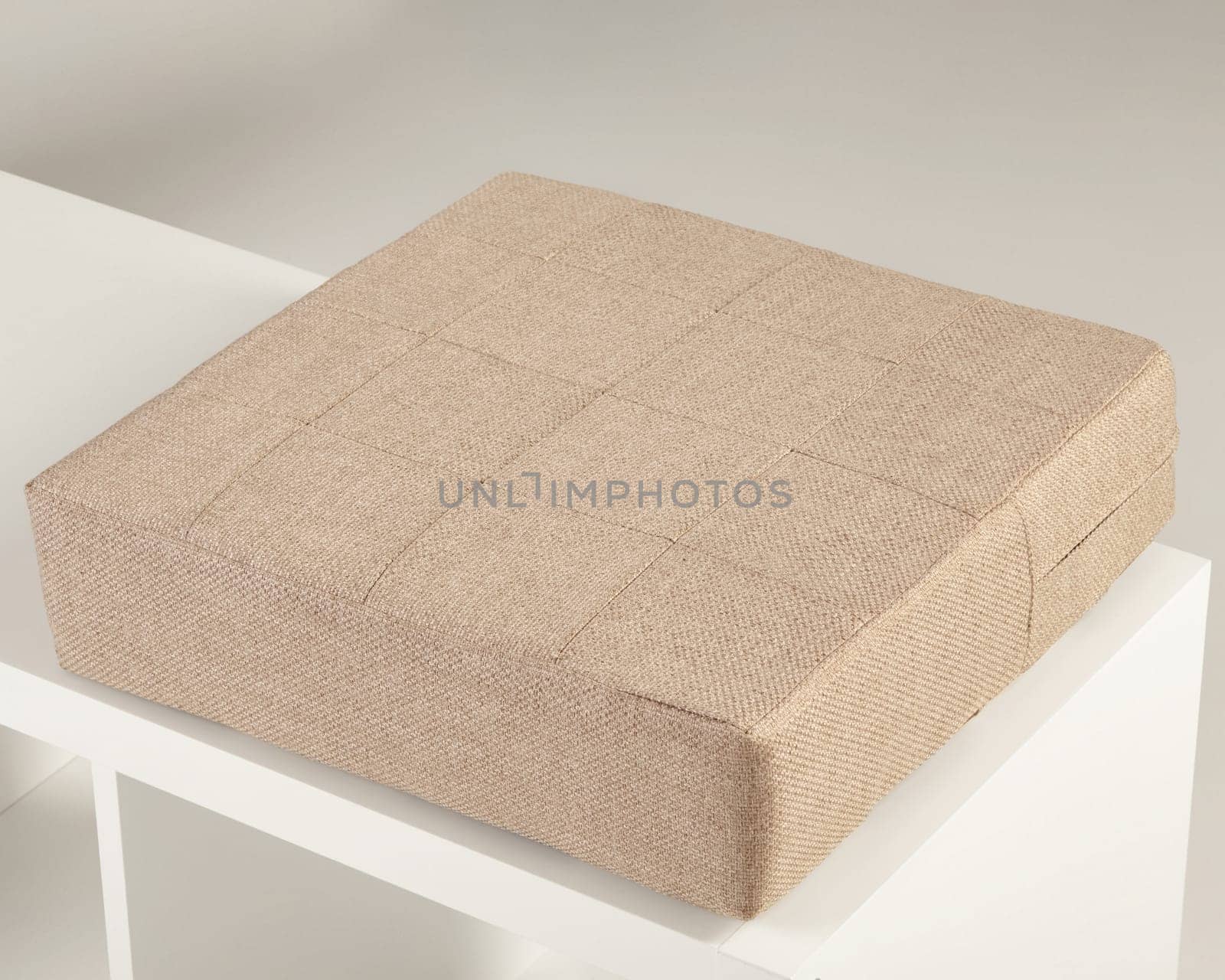 Square beige fabric padded seat cushion resting on a white shelf, offering comfort and style