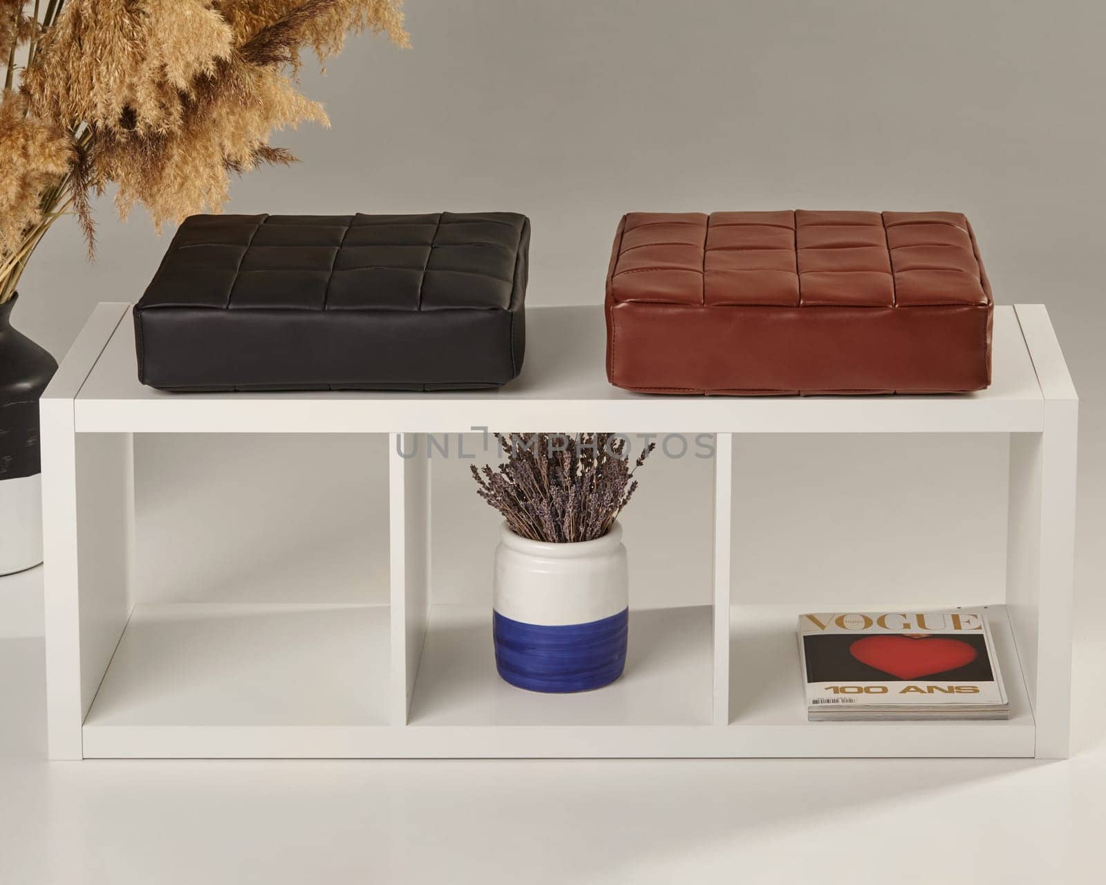 Leather cushions rest on a white shelving unit, showcasing a blend of modern interior design and classic style with a vogue magazine