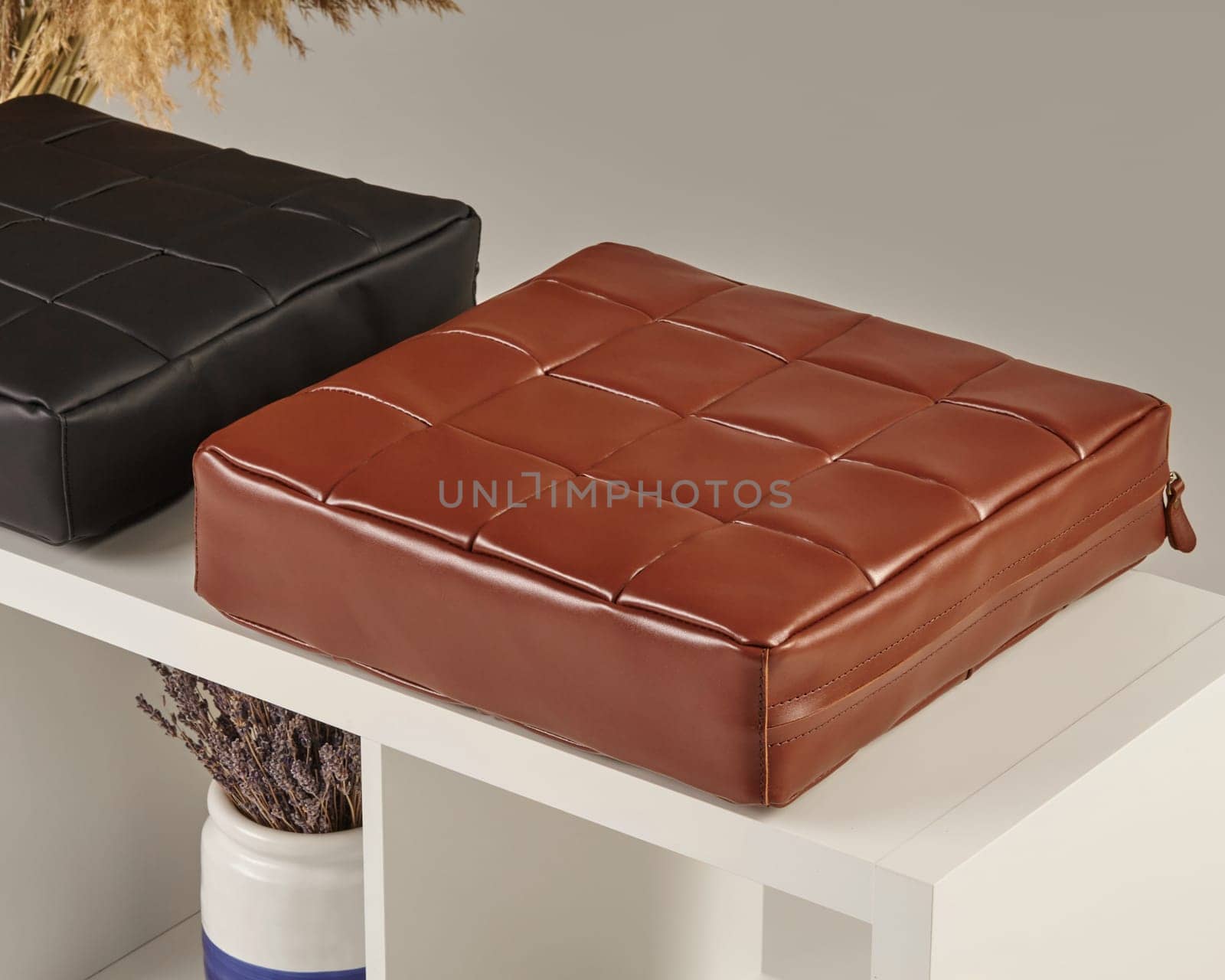 Square, woven leather cushions sit on a white shelf, adding a touch of elegance to a minimalist interior design