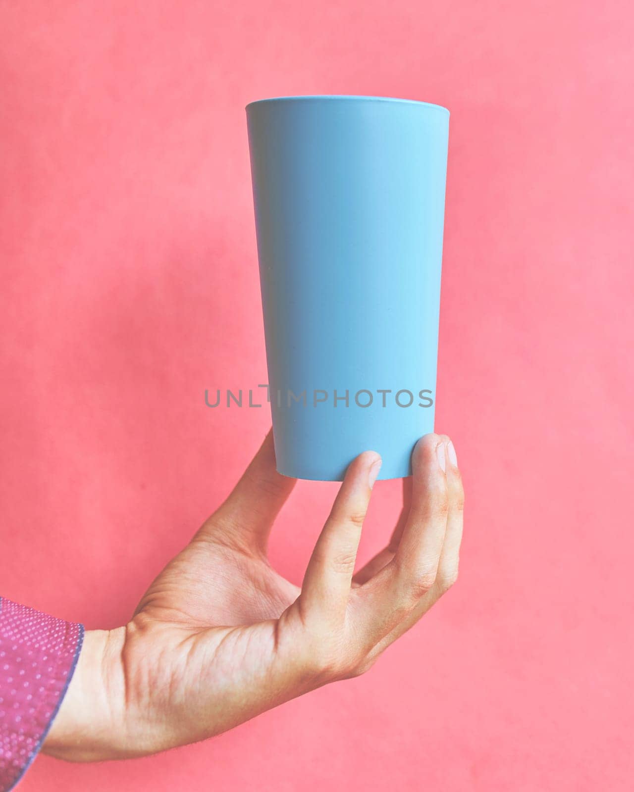 Colorful plastic cup. Plastic blue cup in hand on pink background.