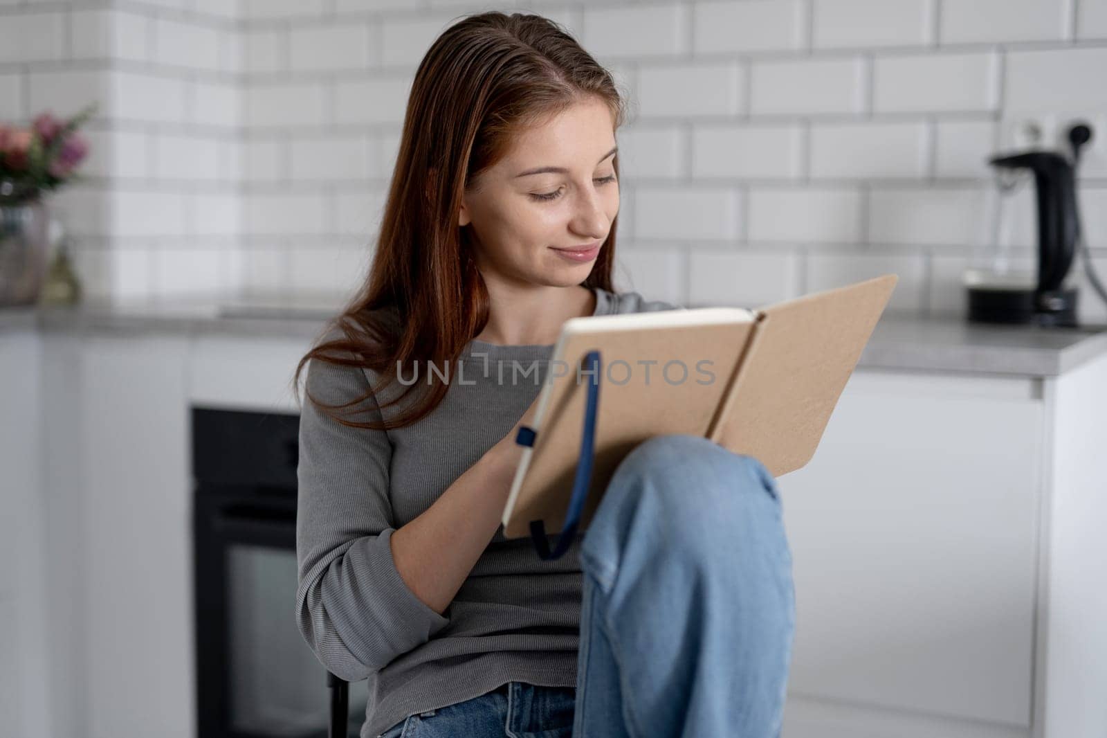 Sweet Teen Girl Reading Notebook Entries While Sitting On A Chair At Home