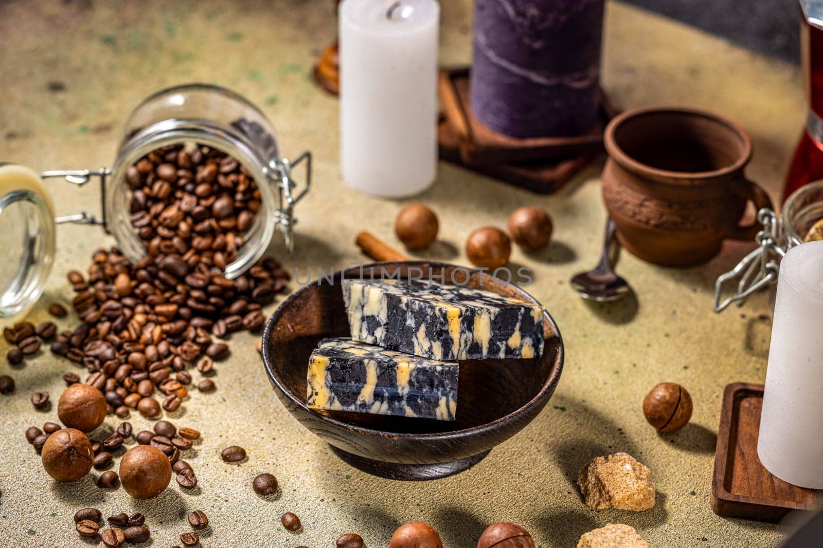 Two slices of marble cheese nestled in a wooden bowl, surrounded by coffee beans, macadamia nuts, candles, and brown sugar, creating a cozy atmosphere