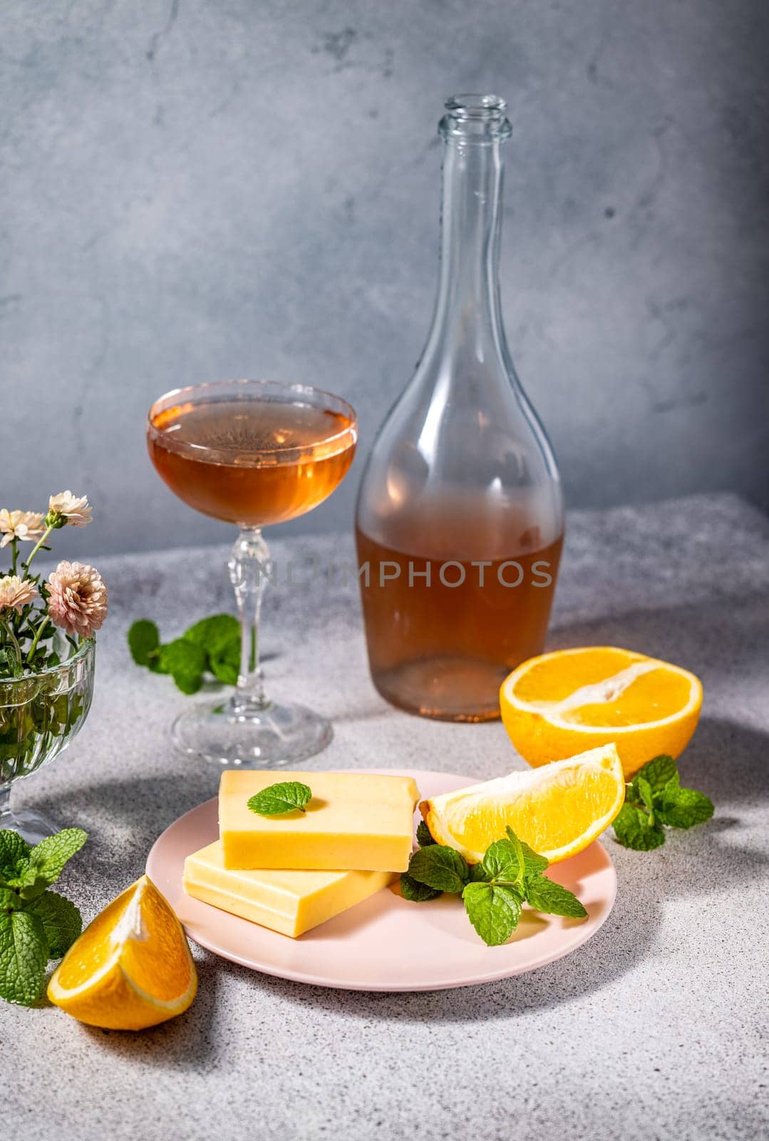 Gourmet cheese slices paired with fresh orange and mint on a pink plate, complemented by a glass and bottle of rose wine