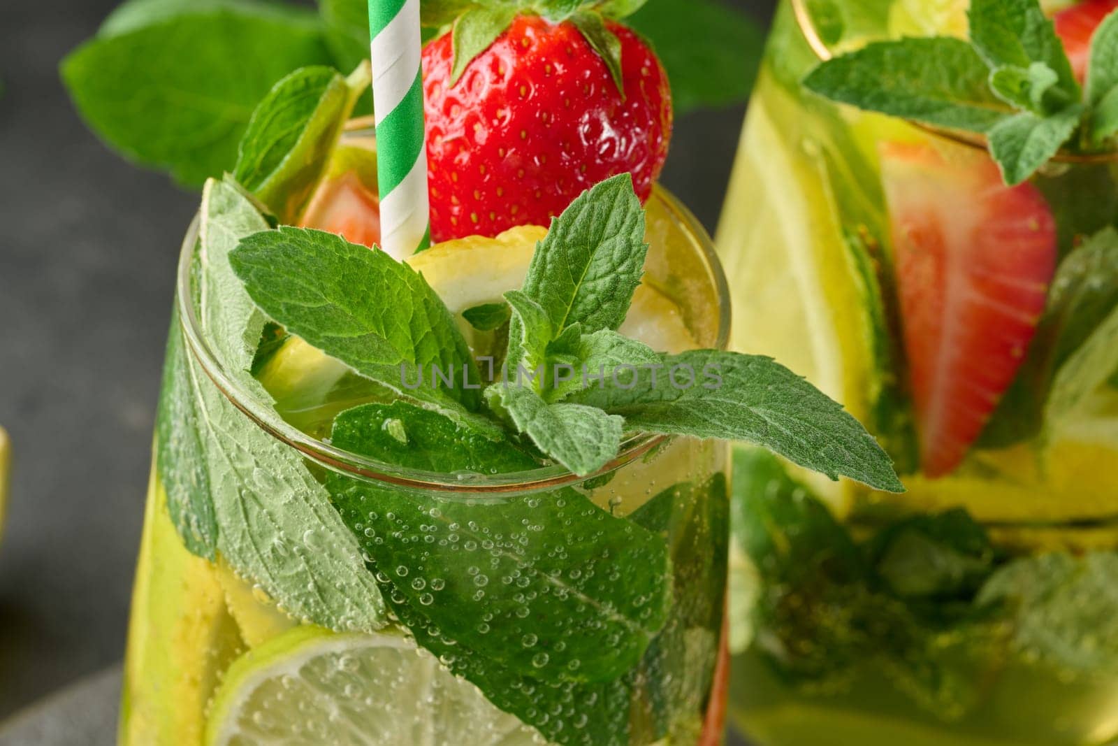 A refreshing drink in a glass with lemon slices, strawberries, fresh mint leaves, and sparkling water, close up