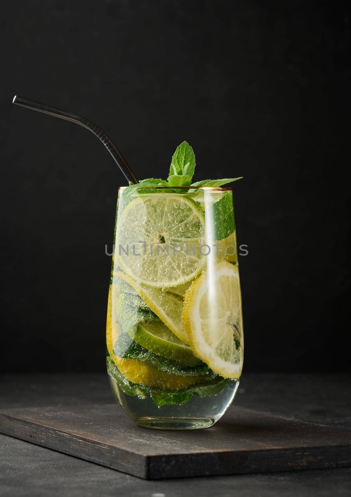 Refreshing detox or summer drink in a glass with lemon, lime, mint, ice, and metal straw. Dark background