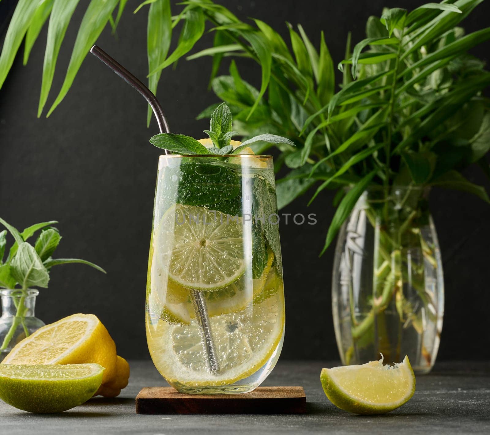 Refreshing detox or summer drink in a glass with lemon, lime, mint, ice, and metal straw. Dark background
