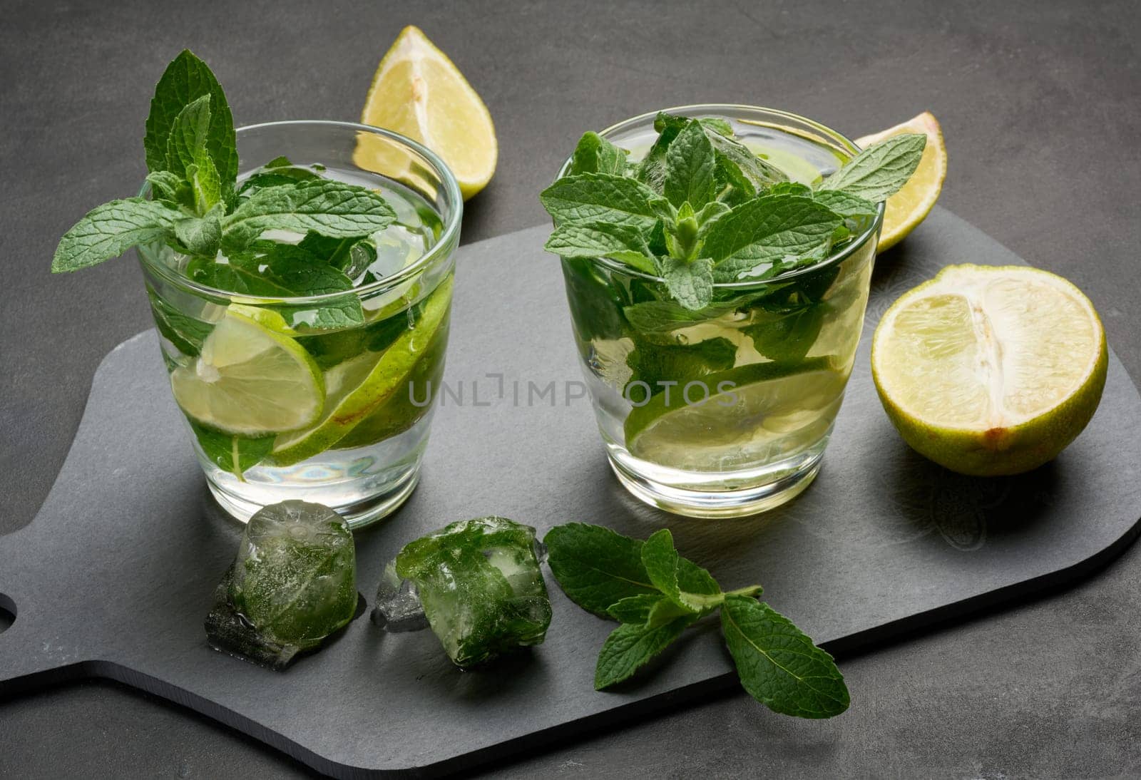 Refreshing mojito cocktail with lime, mint, and ice on dark background, top view