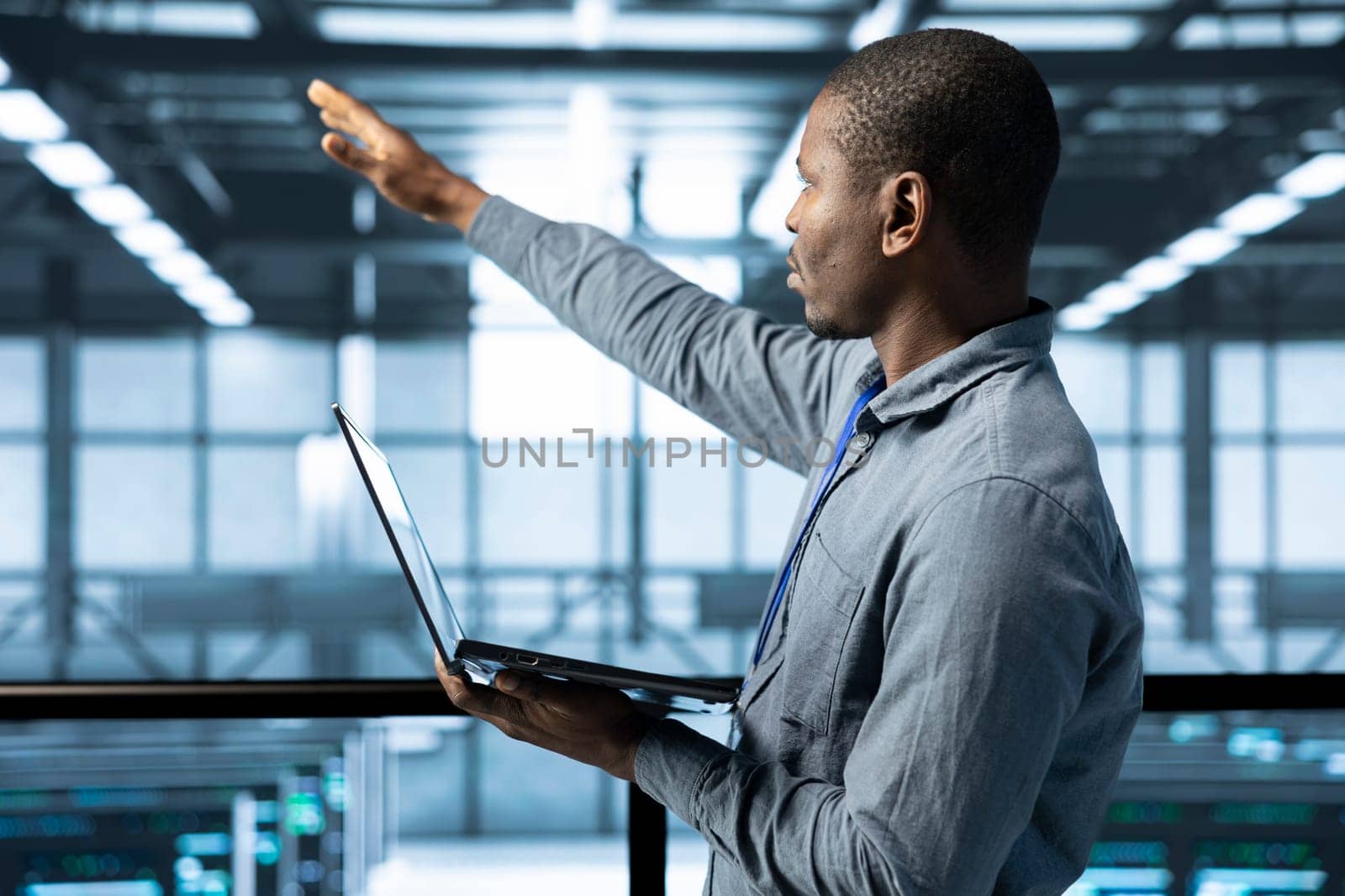 Technician holding laptop, looking around data center, managing server virtualization, finetuning network protocols, verifying high availability configurations, enforcing advanced security measures