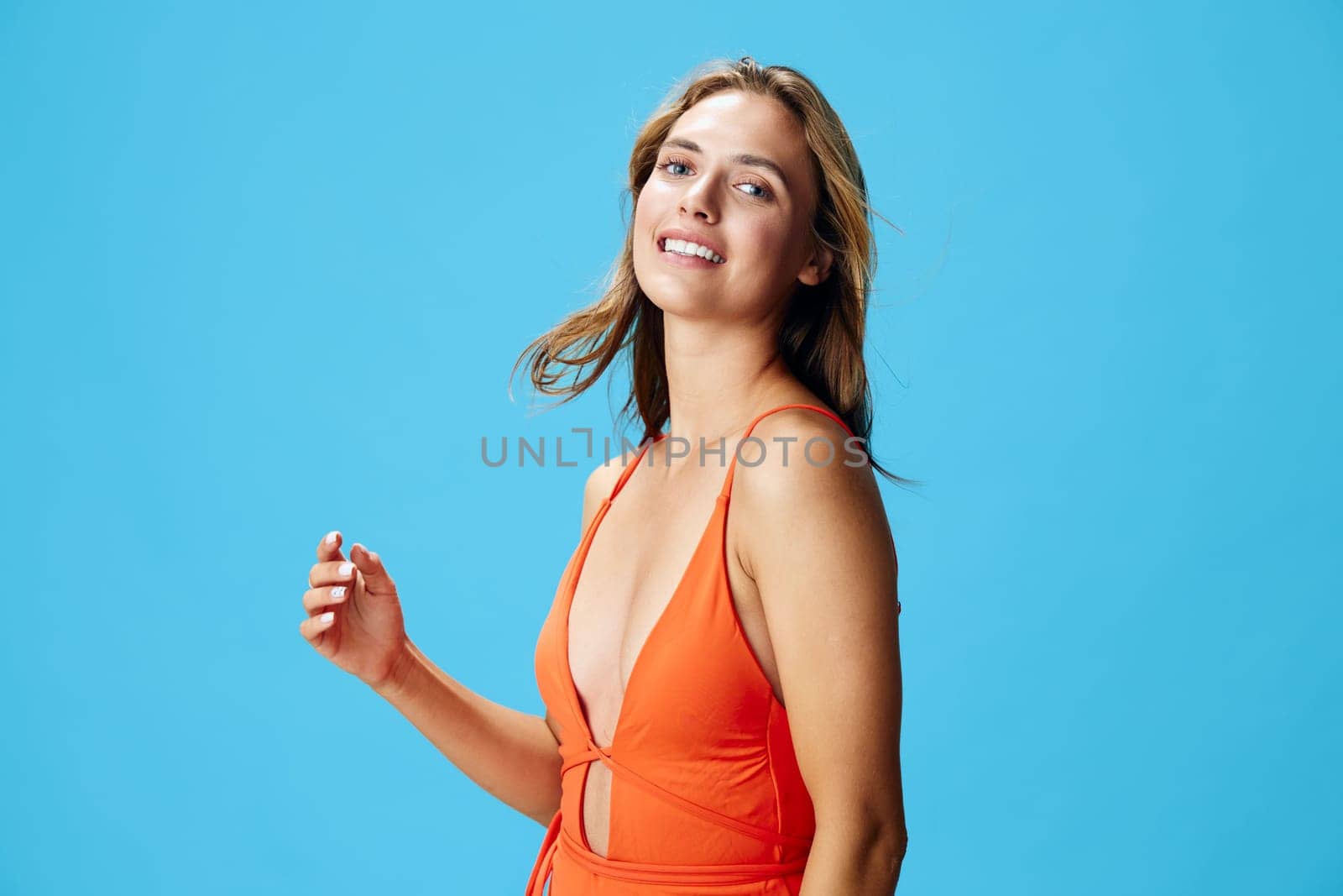 Vibrant woman in bright orange swimsuit striking a pose against a serene blue backdrop