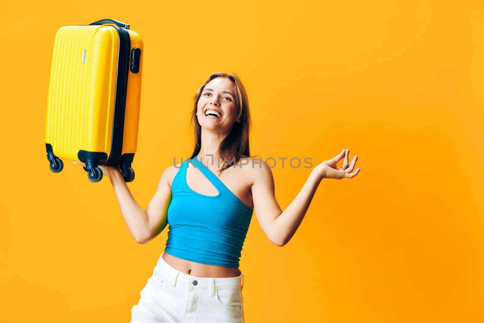 Excited woman joyfully holding a bright yellow suitcase above her head in an outdoor setting